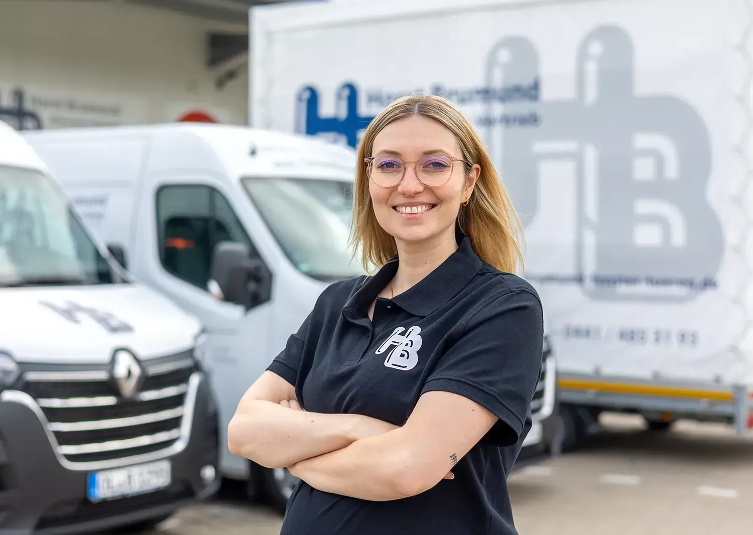 Eine Frau steht mit verschränkten Armen vor einer Reihe von Lieferwagen.