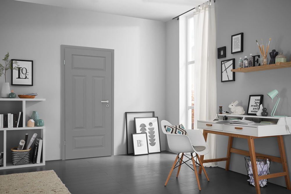 Ein Zimmer mit einem Schreibtisch, einem Stuhl, einem Bücherregal und einer grauen Tür.