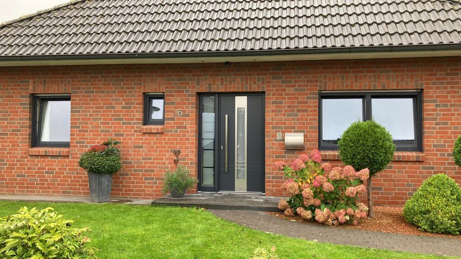 Ein rotes Backsteinhaus mit schwarzer Haustür und schwarzen Fenstern.