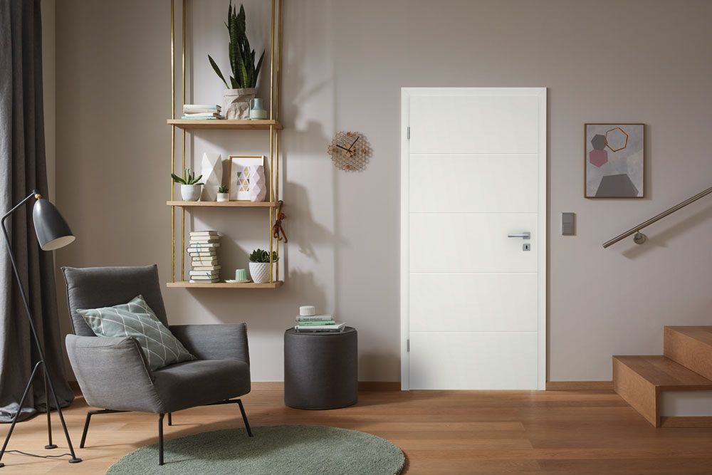 Ein Wohnzimmer mit einer weißen Tür, einem Stuhl, einer Lampe und einer Treppe.