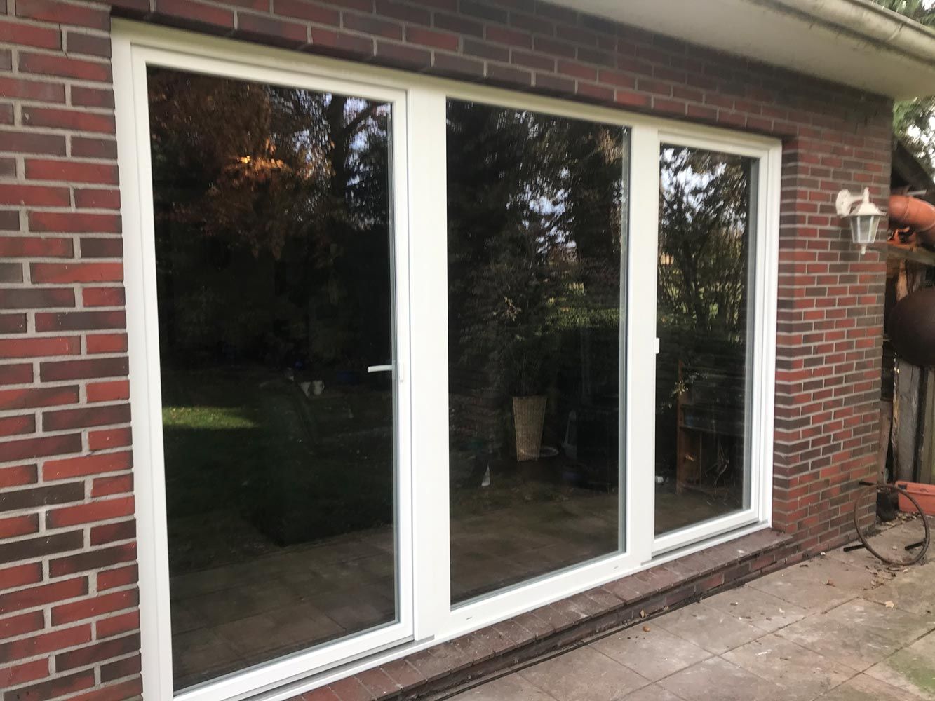 Ein Backsteingebäude mit einer weißen Glasschiebetür, die auf eine Terrasse führt.