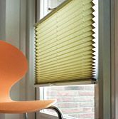 Ein Stuhl steht vor einem Fenster mit Plissee.