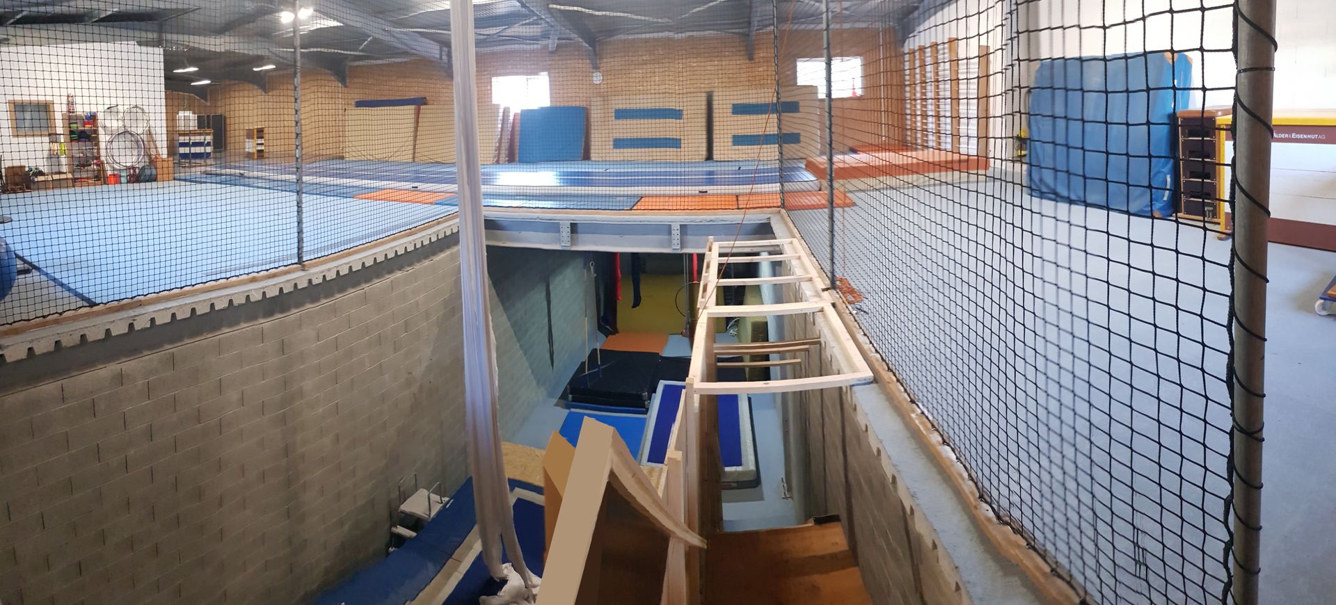 Une personne pratiquant un acrobatie aérienne sur tissu rouge, sous le regard de spectateurs prenant des photos dans une salle de sport.