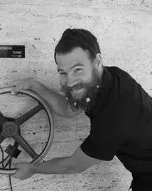 Un homme sourit en faisant tourner une grande roue, à côté d'un mur texturé.