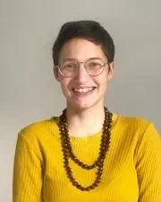 Une femme portant des lunettes et une chemise jaune sourit, arborant un collier de perles.