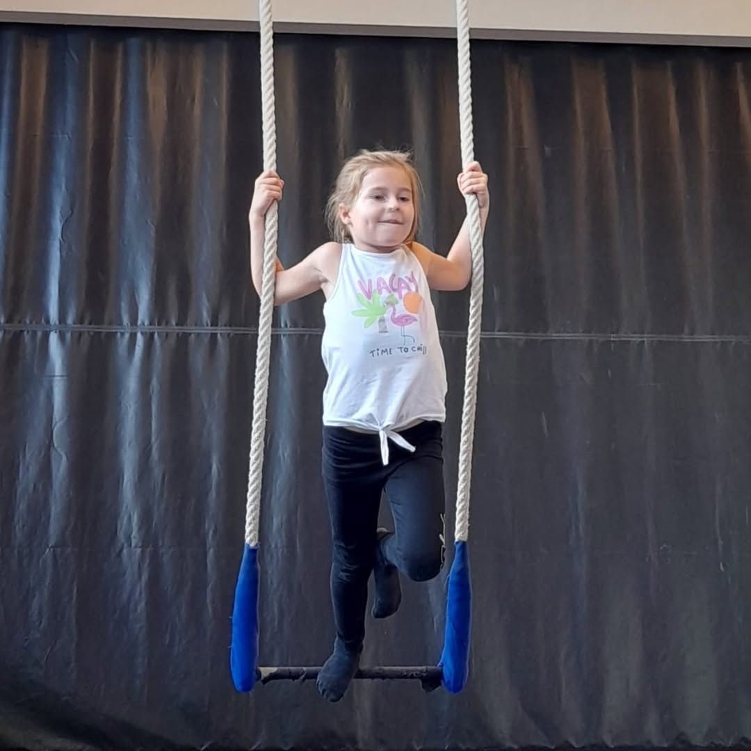 Jeune fille souriante, agrippée à un appareil d'escalade à poignées bleues, en intérieur.