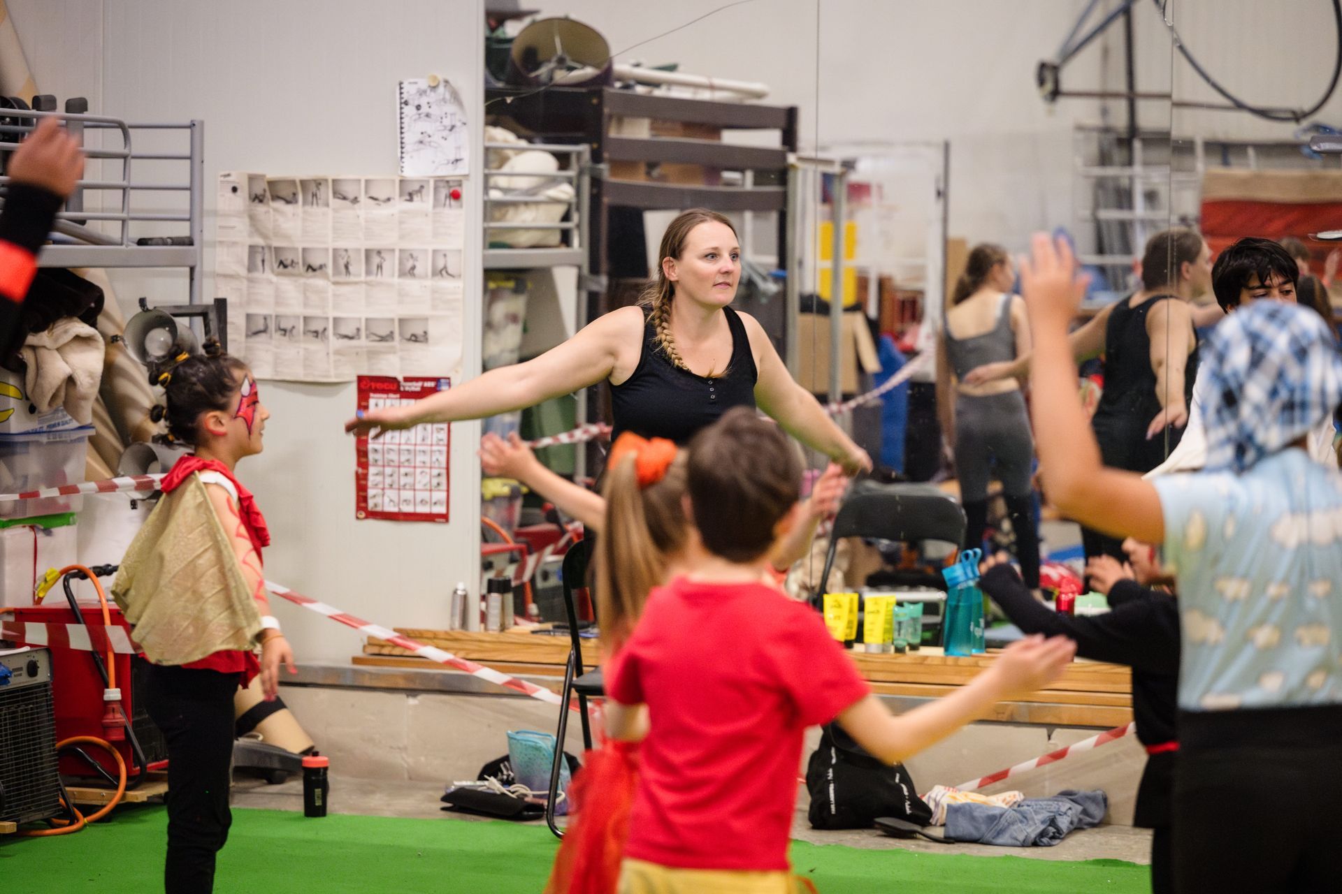 Une personne pratiquant un acrobatie aérienne sur tissu rouge, sous le regard de spectateurs prenant des photos dans une salle de sport.