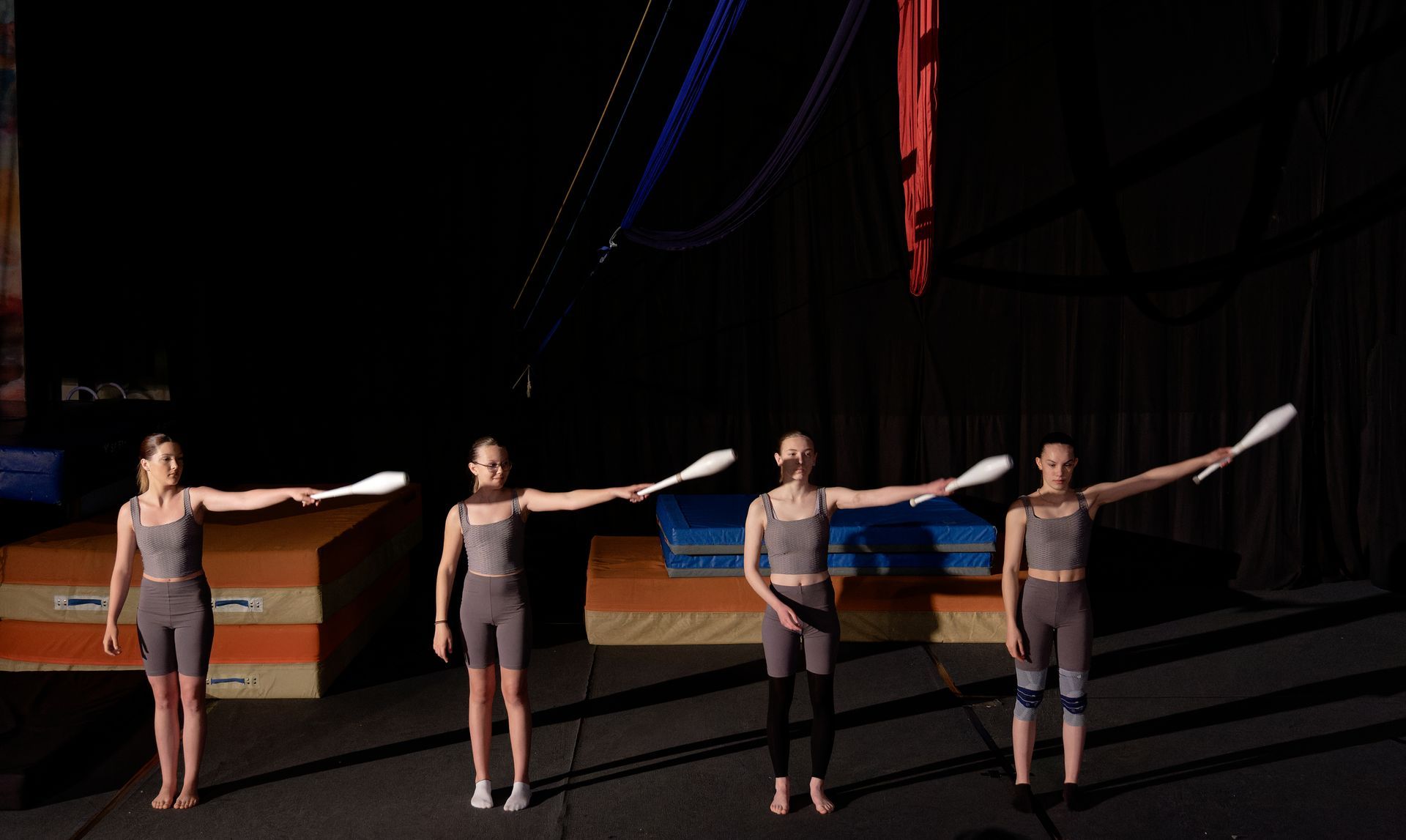 Silhouette d'une personne suspendue à des tissus aériens sur fond bleu avec une lumière vive.