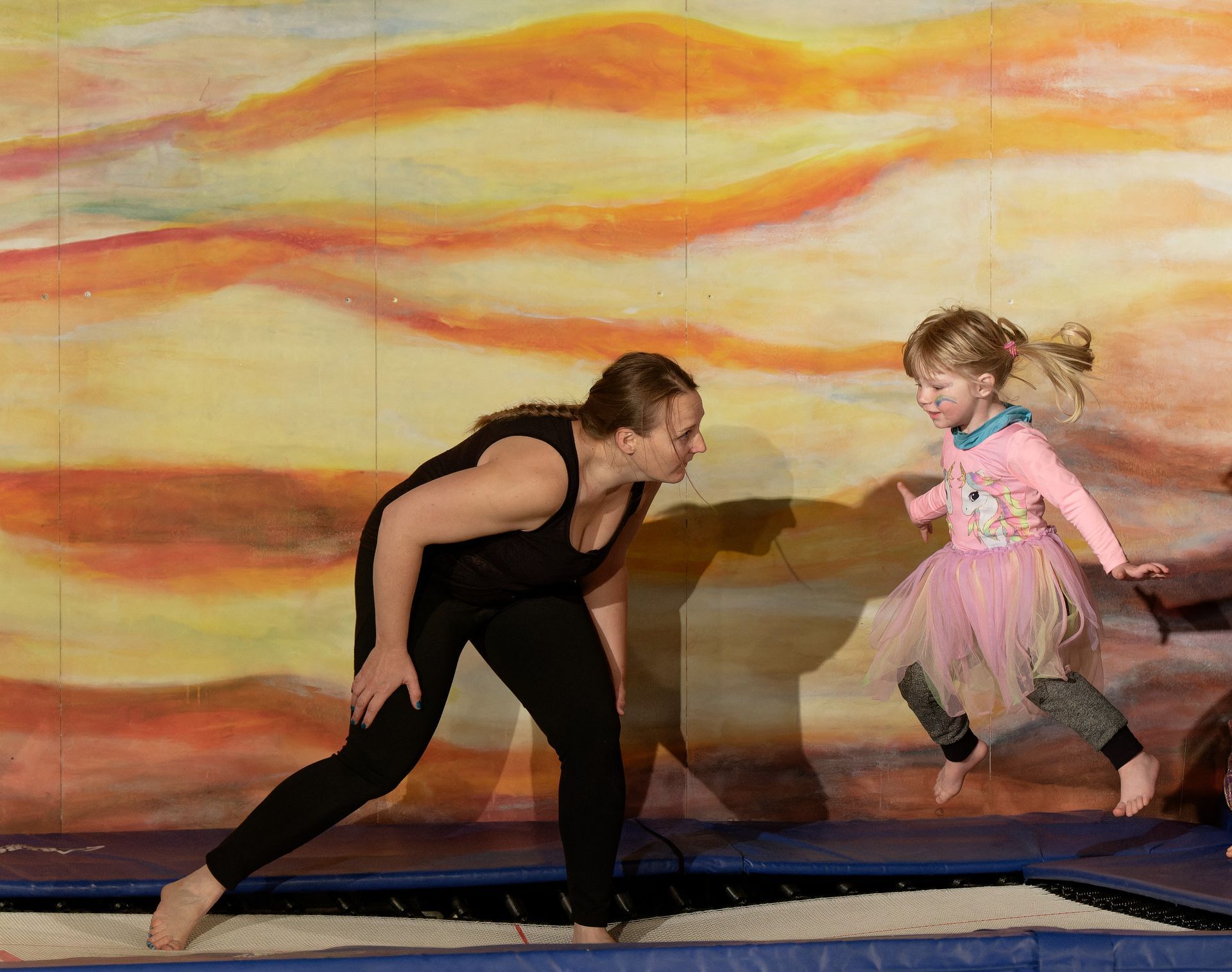 Salle d'entraînement de cirque : une acrobate aérienne dans les airs, d'autres spectateurs au sol ; tapis, cordes et une grande pile de tapis.