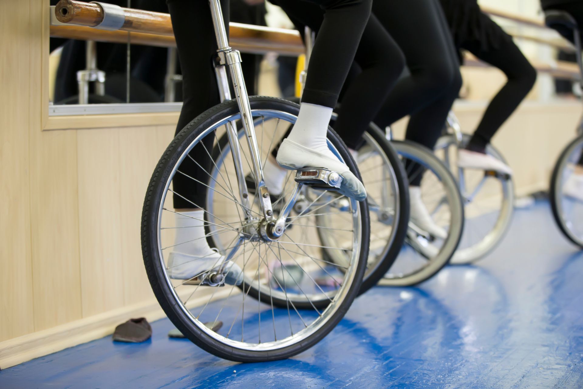 Des personnes sur des monocycles dans une pièce au sol bleu, jambes et pieds visibles.