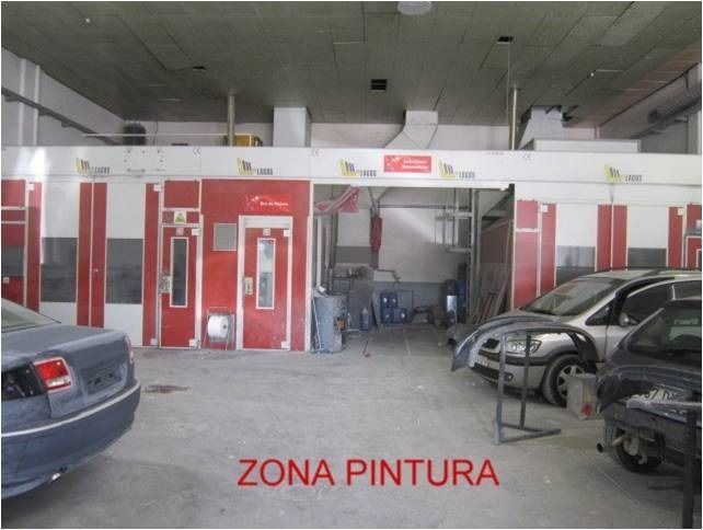 Varios coches están aparcados en un garaje con un cartel que dice zona pintura