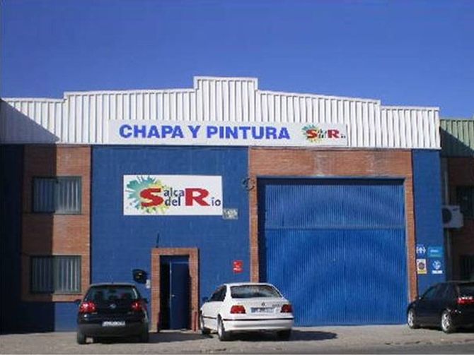 Dos coches están aparcados delante de un edificio de chapa y pintura.