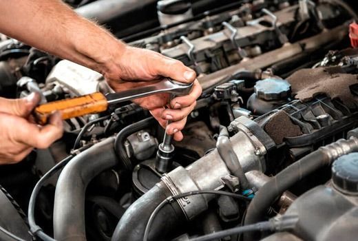 Un hombre está trabajando en el motor de un automóvil con una llave inglesa.