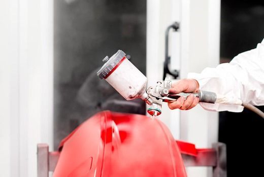 Una persona está rociando pintura sobre un automóvil rojo.