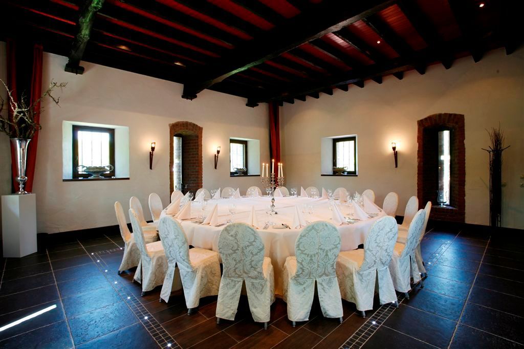 Ronde feesttafel in een rustieke eetkamer met witte stoelhoezen en donkere houten balken.