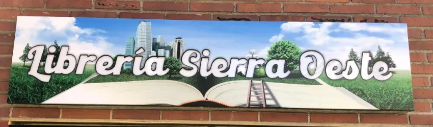 Letrero que dice “Librería Sierra Oeste” en una pared de ladrillo, con un mural de un libro abierto y un gráfico de una torre