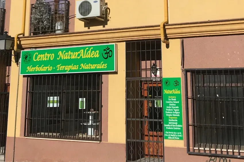 Fachada del centro de terapia herbal Centro NaturaLdea, con un letrero verde en un edificio color beige y ventanas con rejas