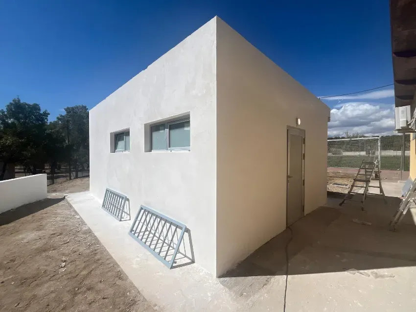 Pequeño edificio blanco de estilo moderno, con ventanas estrechas y una puerta metálica bajo un cielo azul