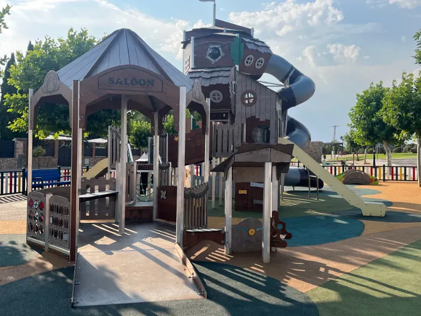 Estructura de juegos de madera con toboganes, rampas y una zona de juegos cubierta en un parque soleado