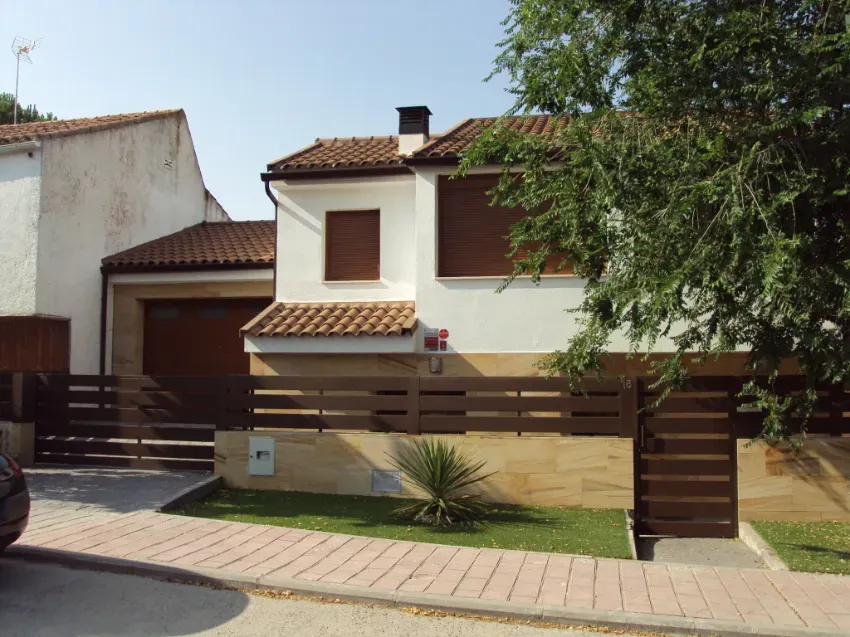 Casa suburbana con fachada marrón y blanca, garaje, cerca delantera y un pequeño jardín ajardinado