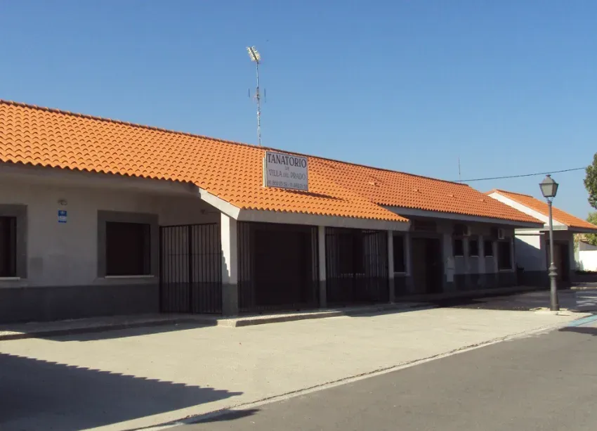 Edificio beige de una sola planta con tejado de tejas naranjas en una calle tranquila bajo un cielo azul despejado