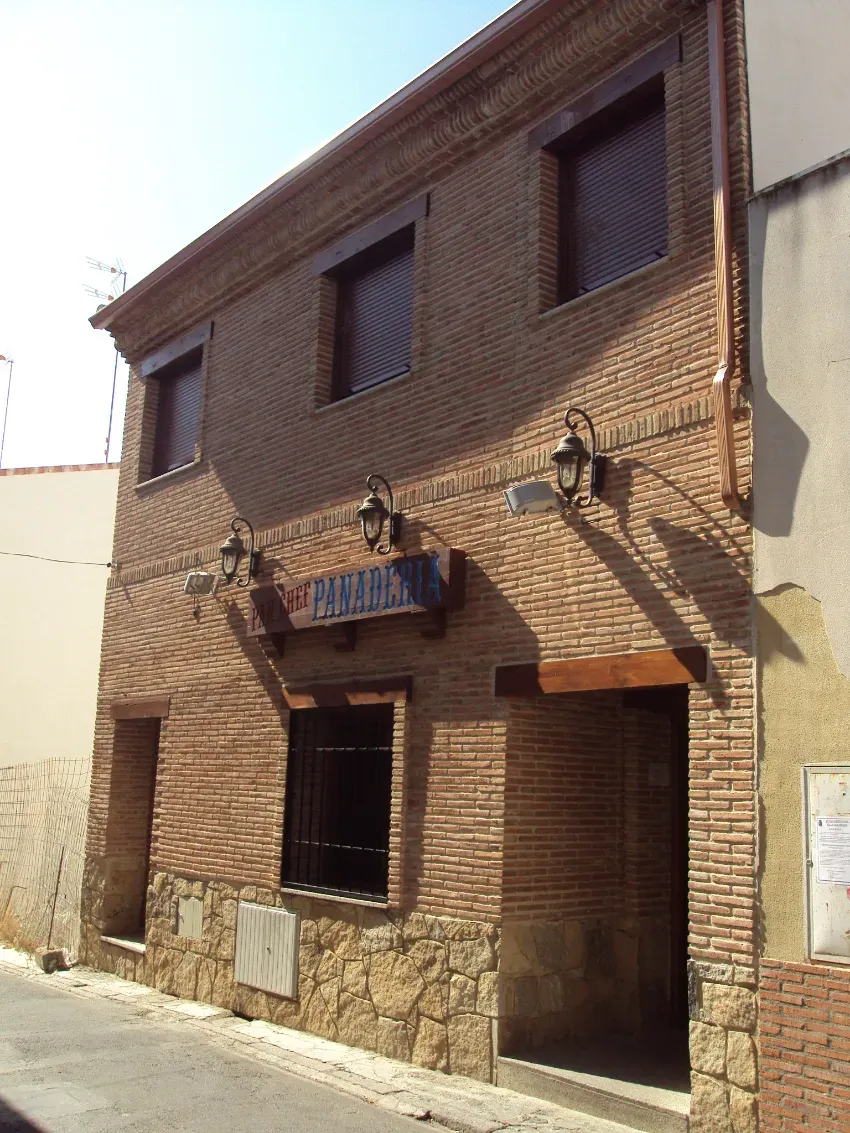 Fachada de ladrillo con dos ventanas en la planta superior, un balcón y una puerta en la planta baja de una calle estrecha