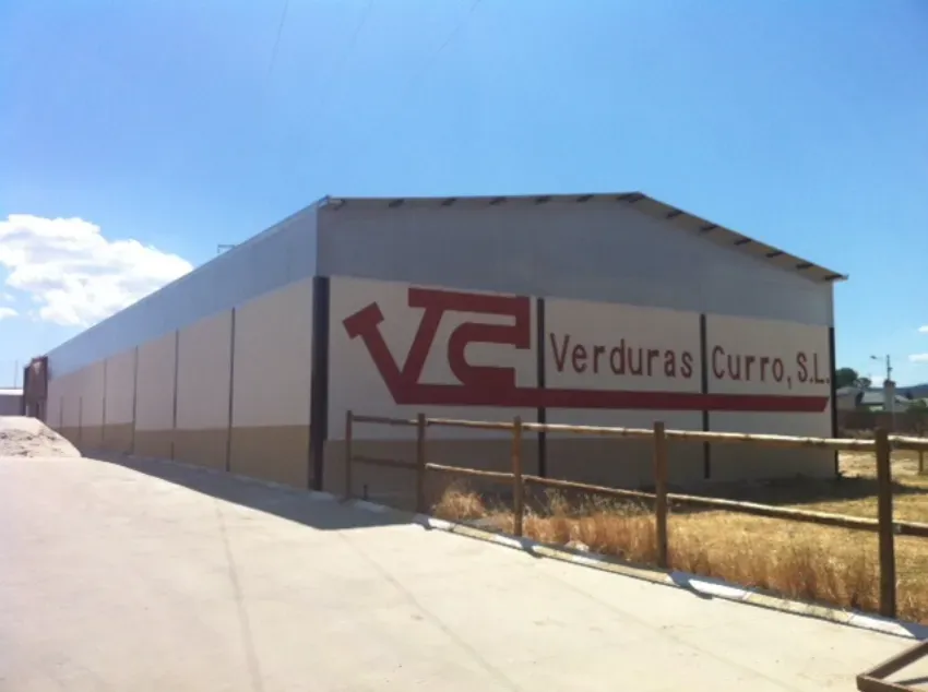 Nave industrial con un letrero de «Verduras Curro, S.L.» bajo un cielo azul despejado