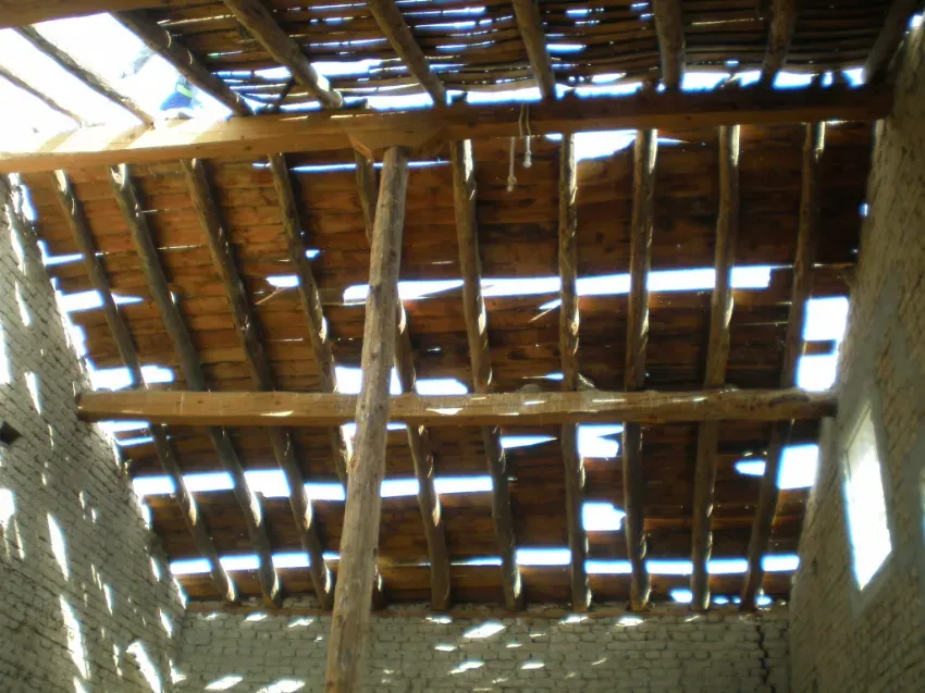 Techo de paja dañado, con huecos por los que entra la luz del día, sobre una pared de ladrillo