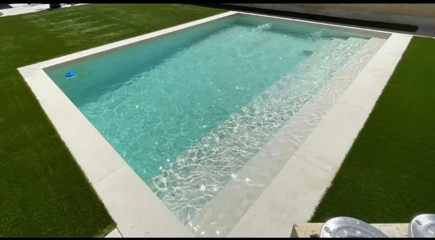 Piscina rectangular al aire libre con agua cristalina, borde blanco y césped artificial verde alrededor