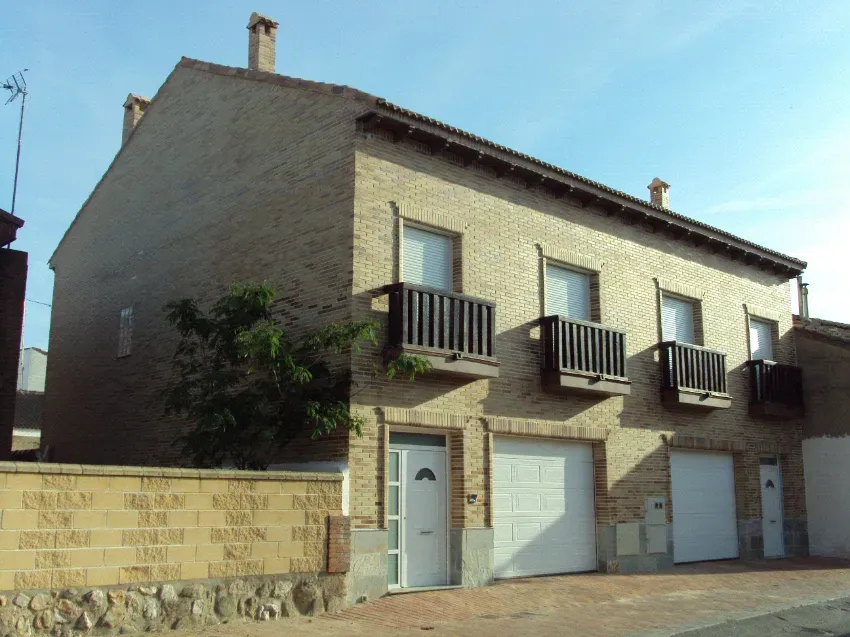 Casa de piedra con puertas de garaje blancas y pequeños balcones bajo un cielo azul