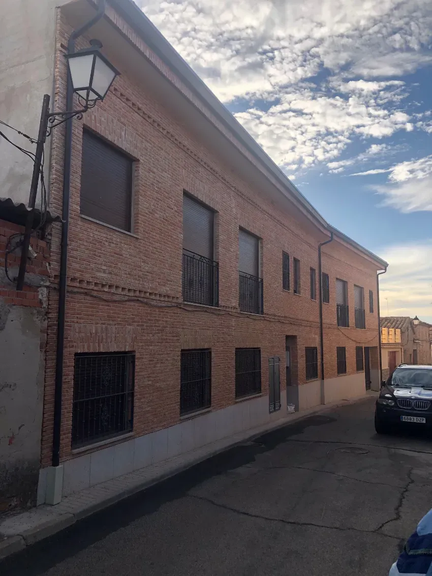 Edificio curvo de ladrillo en una calle estrecha, con ventanas enrejadas y un coche aparcado a la derecha.