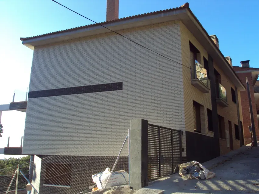 Casas residenciales a lo largo de una estrecha calle en cuesta, con escombros de construcción y una zona vallada delante.