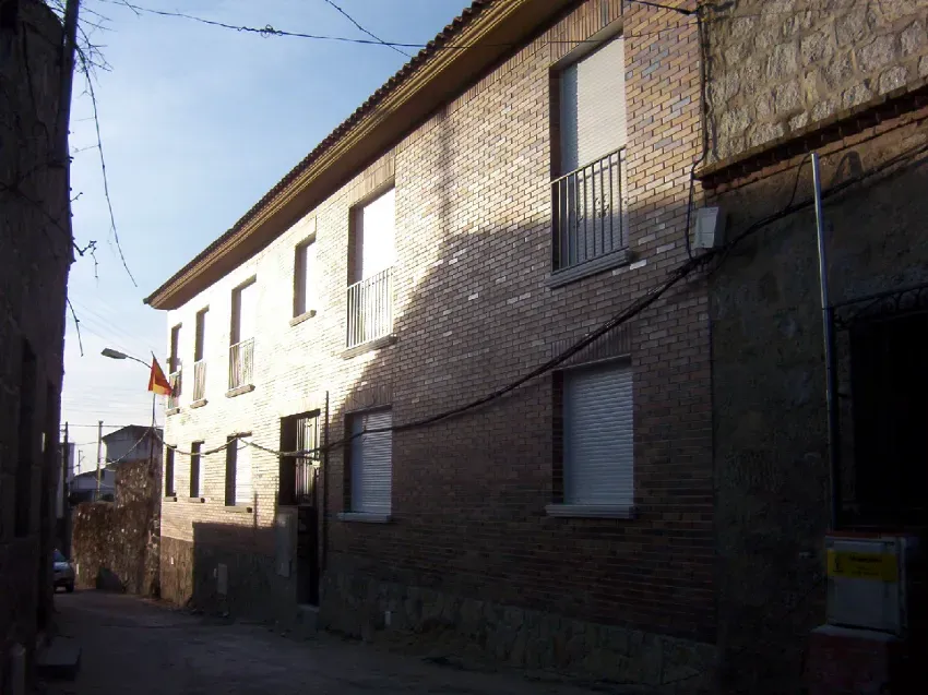 Edificio de apartamentos de ladrillo iluminado por el sol, en una calle estrecha, con ventanas enrejadas y un pequeño callejón