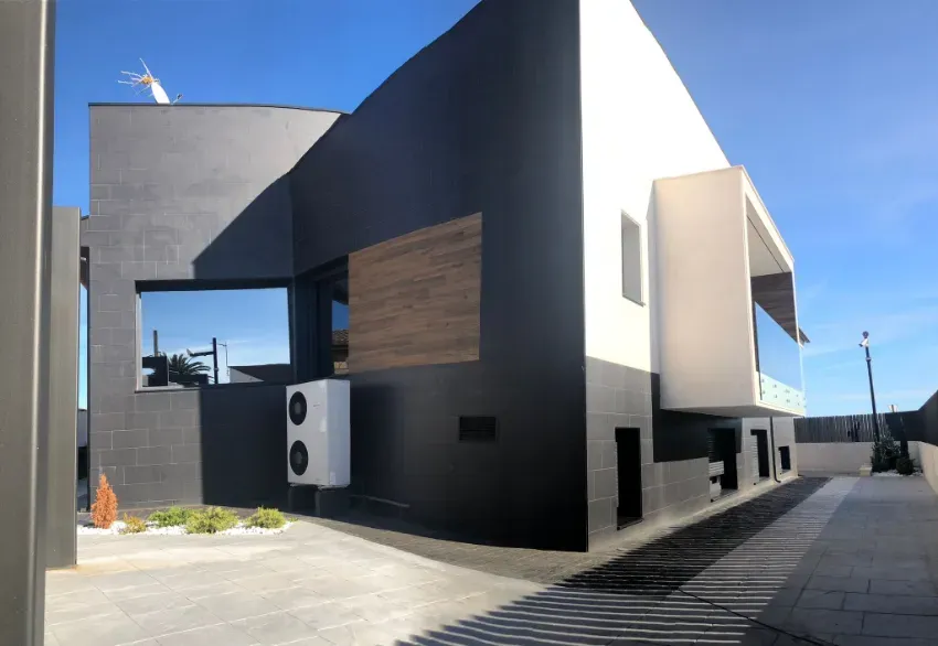 Exterior moderno de una casa en blanco y negro, con diseño geométrico y entrada para vehículos bajo un cielo azul