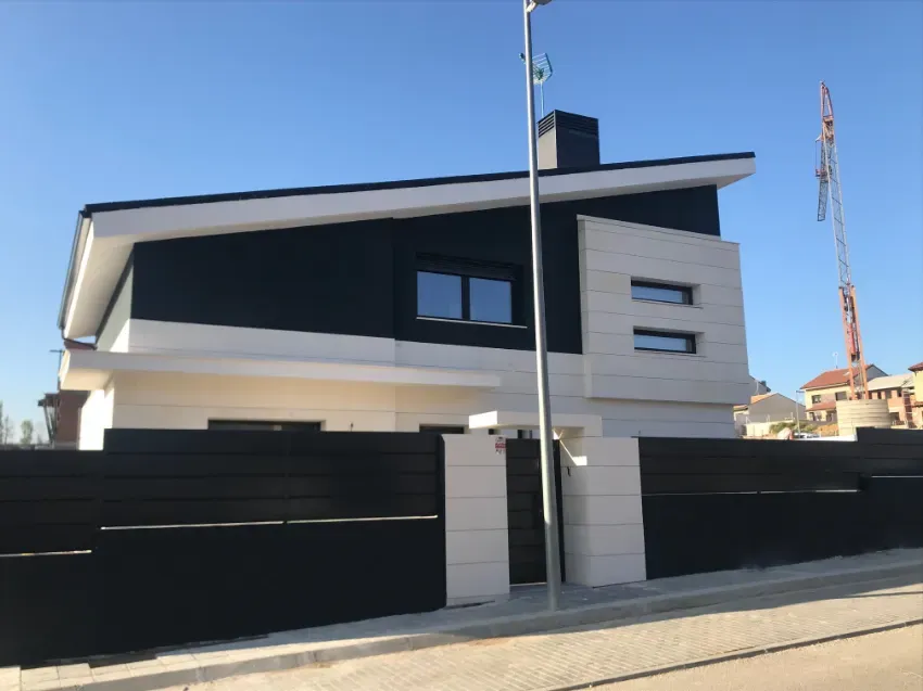 Casa moderna de dos plantas con fachada en blanco y negro, detrás de una valla negra y bajo un cielo azul despejado