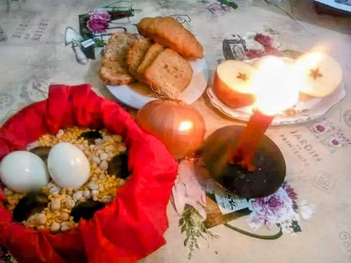 Velas encendidas y huevos sobre un paño floral junto a pan y una granada para un ambiente ritual.