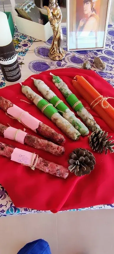 Paquetes de telas enrolladas de colores sobre una tela roja, con una piña y elementos decorativos al fondo.