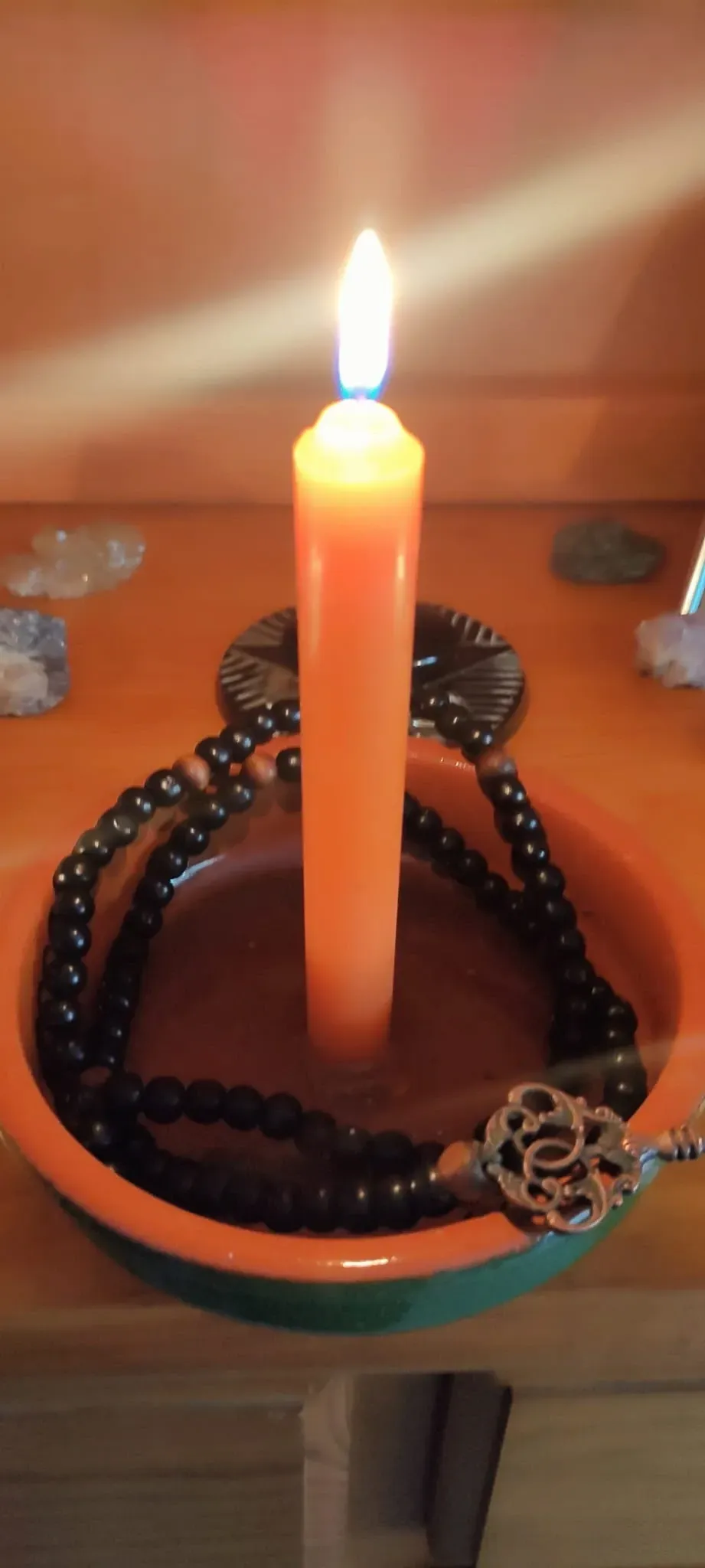 Vela alta encendida en un plato de cer&aacute;mica con ornamento al rededor. 