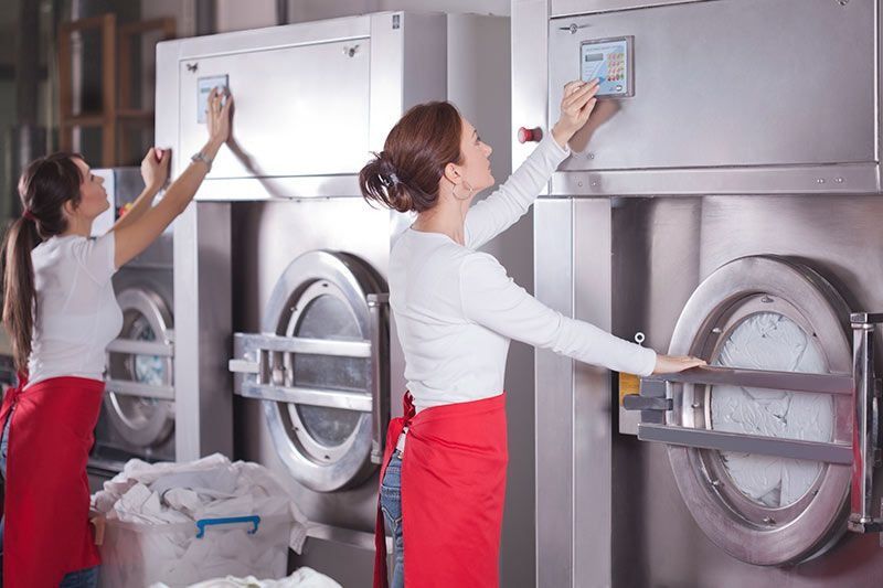 Dos mujeres están trabajando en lavadoras en una lavandería.