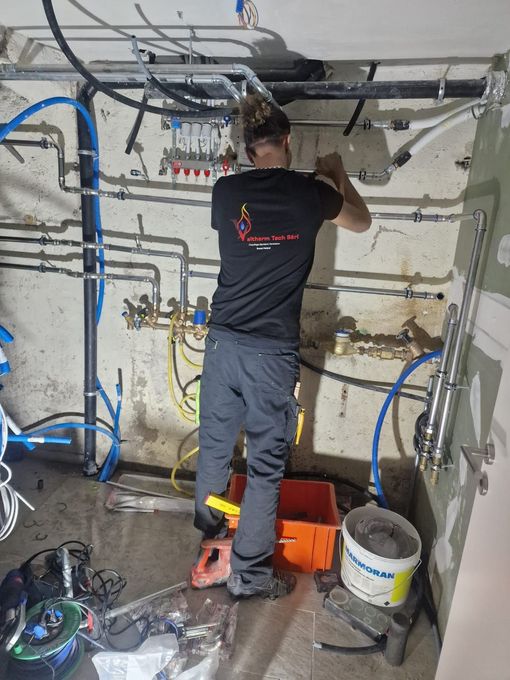 Un plombier travaille sur une chaudière avec une clé et un tournevis.