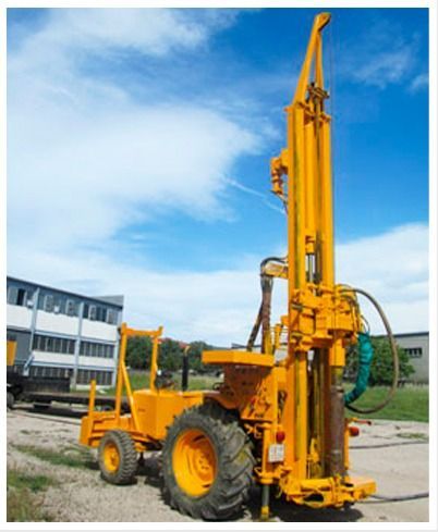 Plataforma de perforación amarilla sobre ruedas frente a un edificio, bajo un cielo azul.