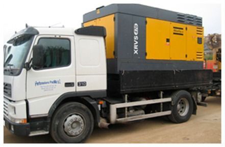 Camión blanco que transporta un generador industrial amarillo y negro en un entorno al aire libre.