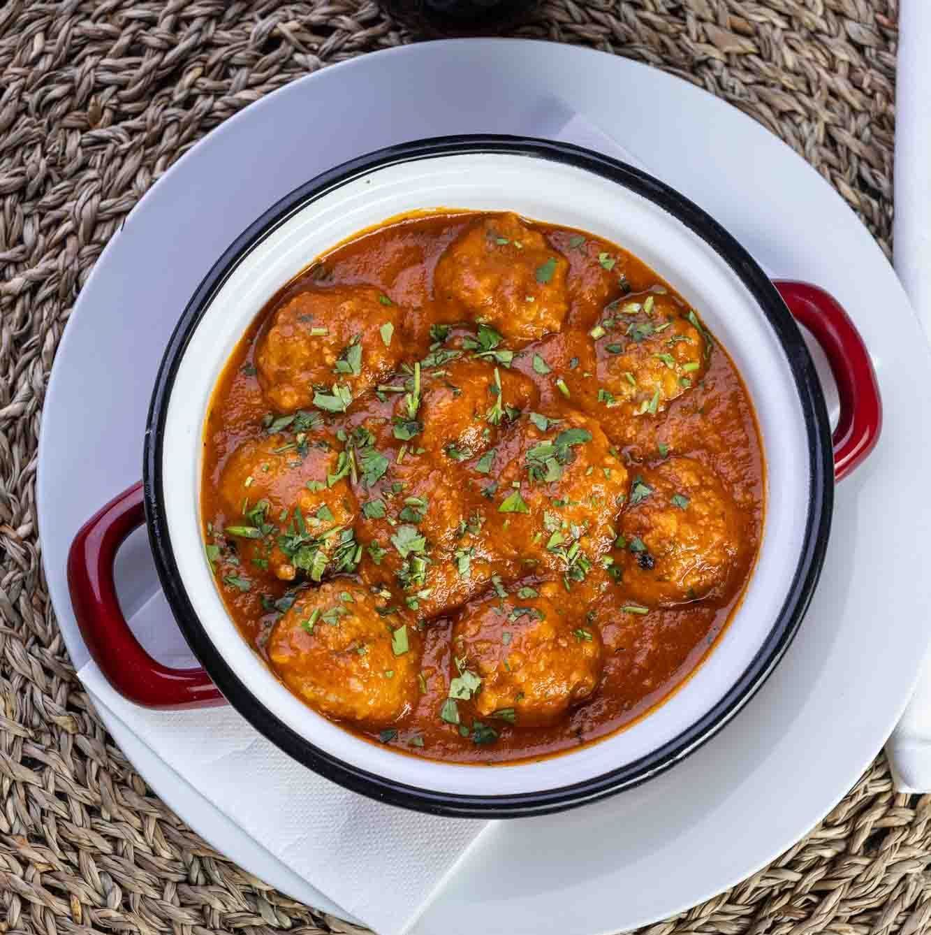 Un tazón de albóndigas en salsa con asas rojas en un plato blanco.