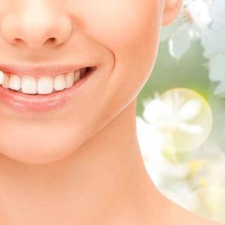 Un primer plano del rostro de una mujer sonriendo con flores en el fondo.