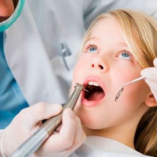 A una niña le están examinando los dientes un dentista.