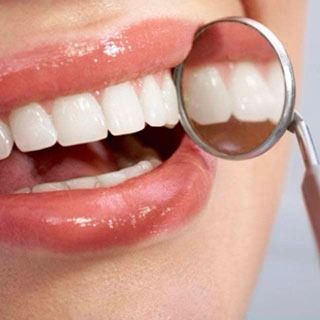 Una mujer se hace examinar los dientes por un dentista con un espejo.