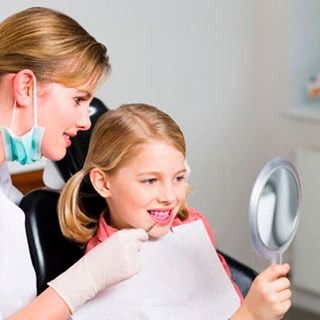 Un dentista mira los dientes de una niña en un espejo.