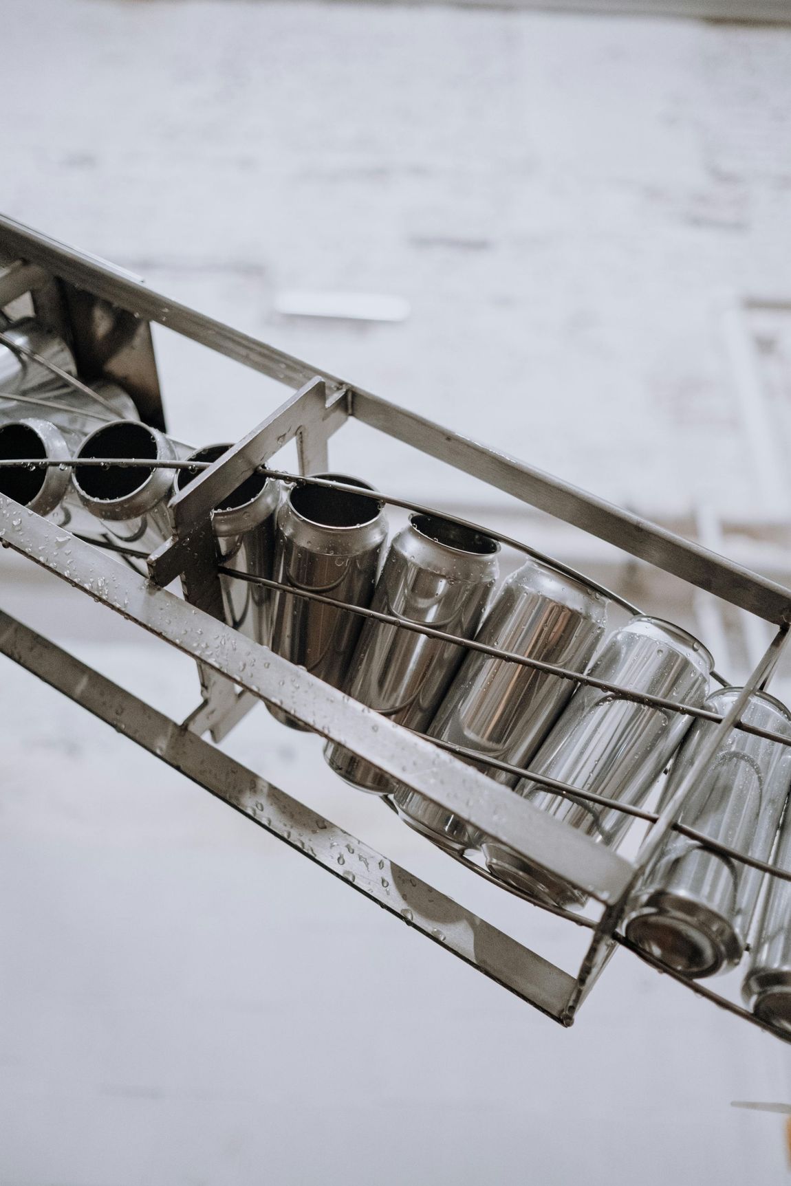 Una serie de latas de aluminio vacías para bebidas se desplazan en fila a lo largo de una cinta transportadora metálica industrial inclinada.