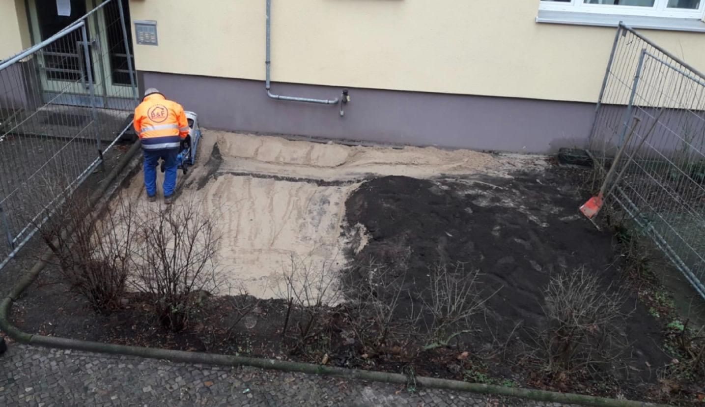 Ein Arbeiter bedient eine Maschine bei Arbeiten auf dem Boden außerhalb eines Gebäudes, in einem umzäunten Bereich