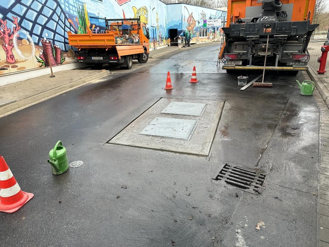 Straßenbauarbeiten im Gange: LKW, orangefarbener LKW, Leitkegel, offene Zufahrt zu Versorgungsleitungen 